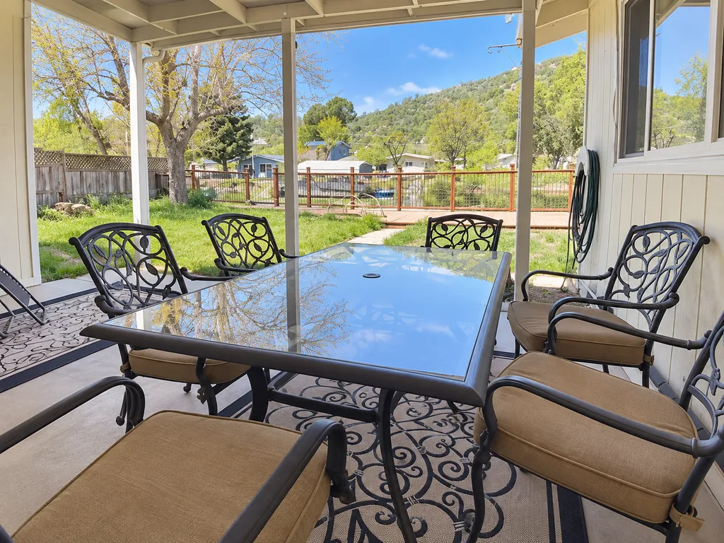 Covered patio with a glass table and chairs, a grassy yard, and a tree.