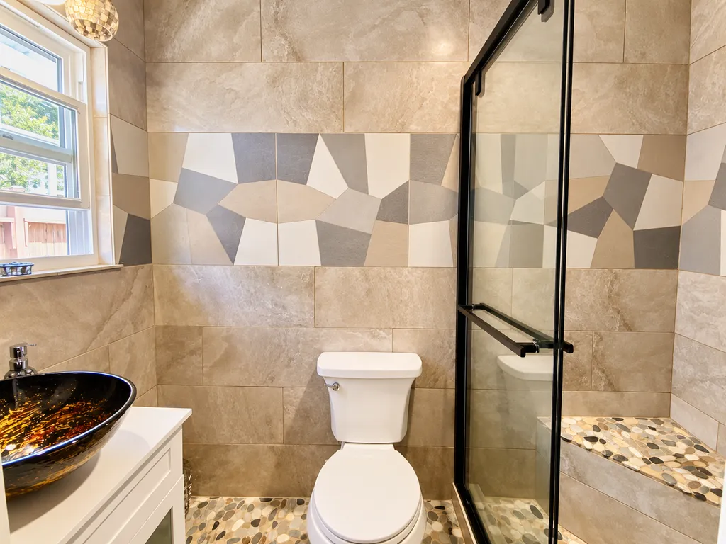 A bathroom with a white toilet, a glass shower, and a patterned tile wall.